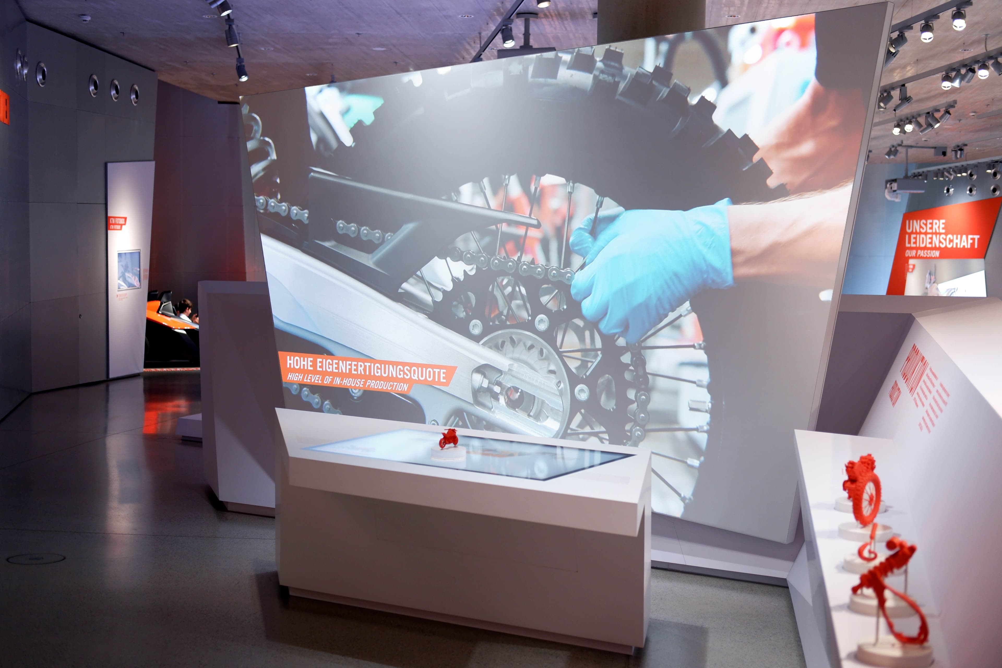 Overview of the exhibit: table with token placed on it, in the background a video of the assembly of a motorcycle